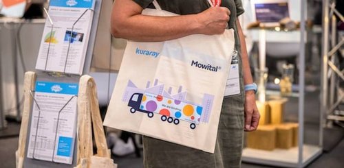 Trade fair visitor Ceramitec 2022 with cotton bag showing the logos of Kuraray and Mowital and a truck in corporate identity colors.