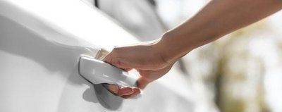 Hand on the door handle of a white car.